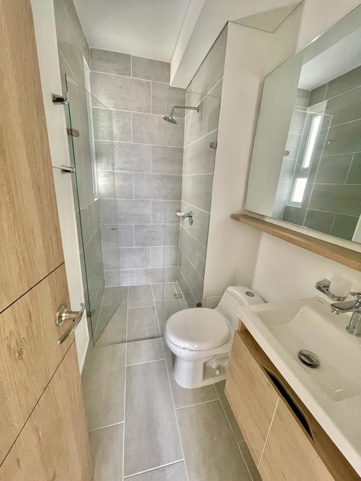 Baño con ducha de vidrio, sanitario y lavamanos con espejo